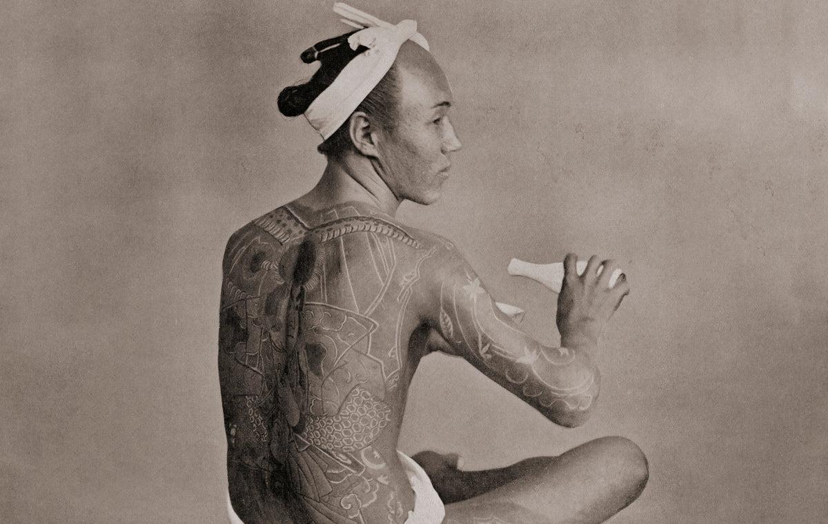 Vintage photograph of a heavily tattooed man seated, from the history of tattooing