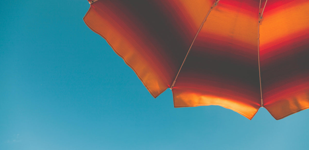 A beach umbrella against a clear blue sky, sun safety for tattooed skin