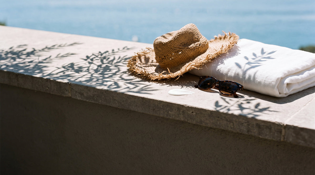 A straw hat, linen towel and a pool of white lotion on a sunlit terrace ledge, sunscreen lotion for tattoos