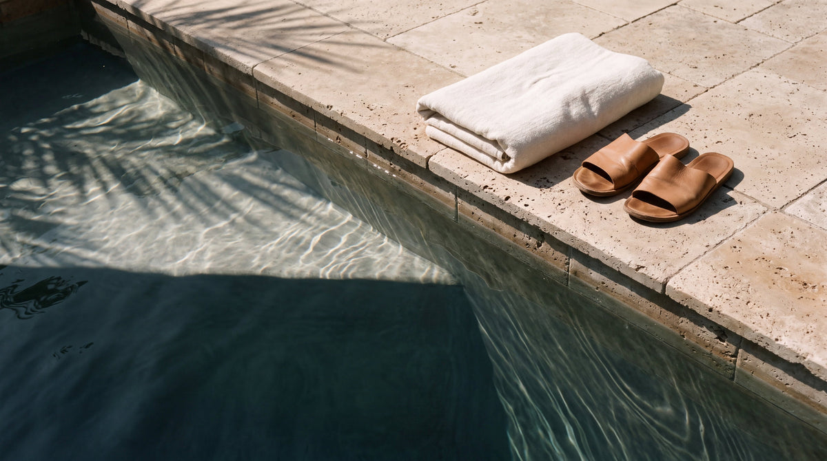 A folded towel and leather slides at the edge of a sunlit pool, when it is safe to swim with a new tattoo