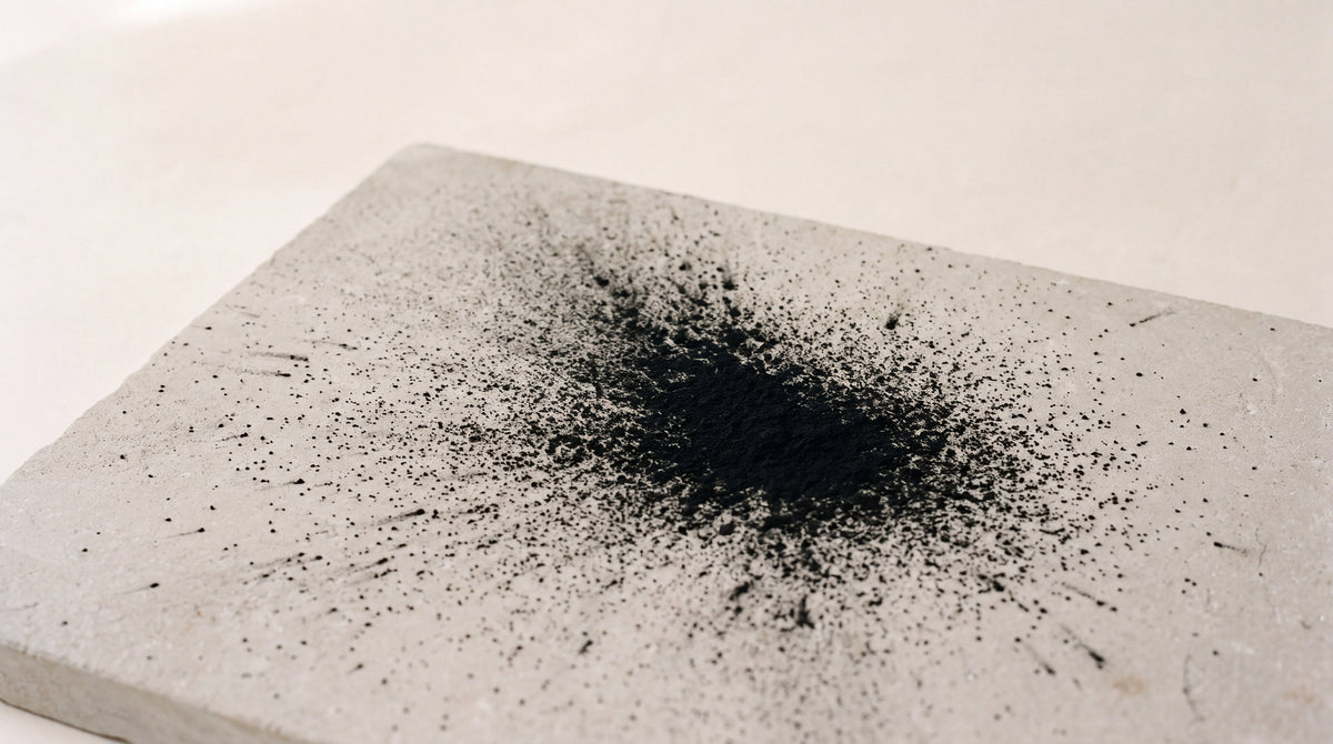 Fine black pigment granules scattered across pale blue paper, dispersing outward from a dense central mass