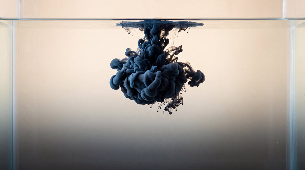 Dark ink blooming through clear water in a glass tank, the science of why tattoos are permanent