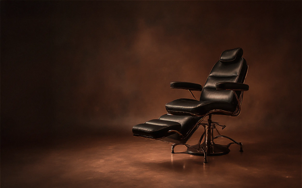 An empty black leather tattoo chair in warm studio light, where the SKINGRAPHICA story began